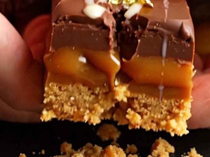 A close-up of a stack of three-layer Millionaire's shortbread squares with gold leaf garnish.