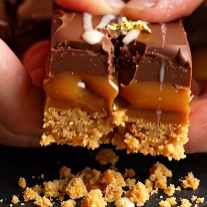 A close-up of a stack of three-layer Millionaire's shortbread squares with gold leaf garnish.