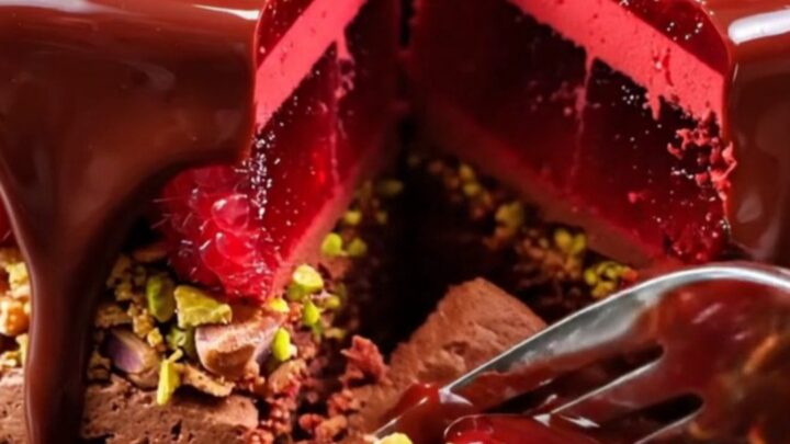 A glossy dark chocolate mirror glaze entremet with visible raspberry and pistachio layers.