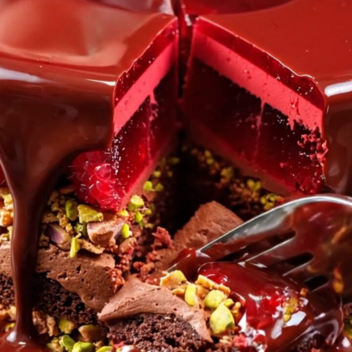 A glossy dark chocolate mirror glaze entremet with visible raspberry and pistachio layers.