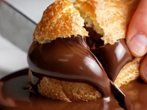 A close-up shot of a chocolate eclair with a glossy ganache top, showing a bite taken out to reveal creamy filling.
