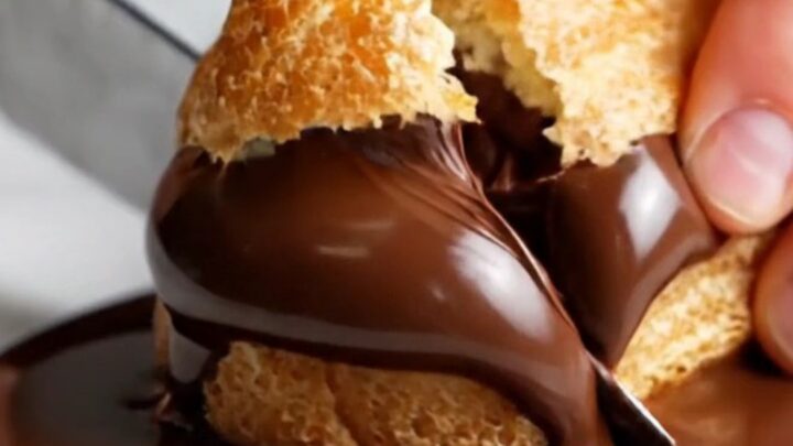 A close-up shot of a chocolate eclair with a glossy ganache top, showing a bite taken out to reveal creamy filling.