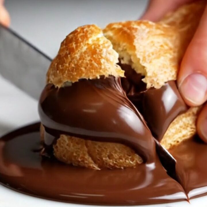 A close-up shot of a chocolate eclair with a glossy ganache top, showing a bite taken out to reveal creamy filling.