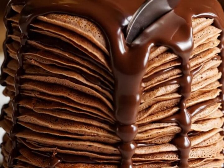 A towering twenty-layer chocolate crepe cake with visible hazelnut cream layers and a glossy dark chocolate ganache glaze.
