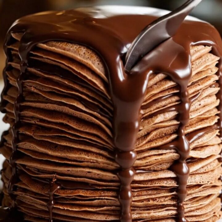 A towering twenty-layer chocolate crepe cake with visible hazelnut cream layers and a glossy dark chocolate ganache glaze.