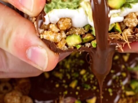 A close-up shot of a square of pistachio rice krispie treat being pulled apart, showing gooey marshmallow and crunchy layers.