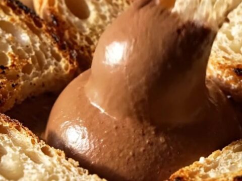 A close-up of dark chocolate mousse drizzled with olive oil and topped with flaky sea salt.