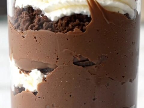 A close-up shot of a glass cup filled with layers of crushed Oreos, dark chocolate pudding, and glossy ganache.