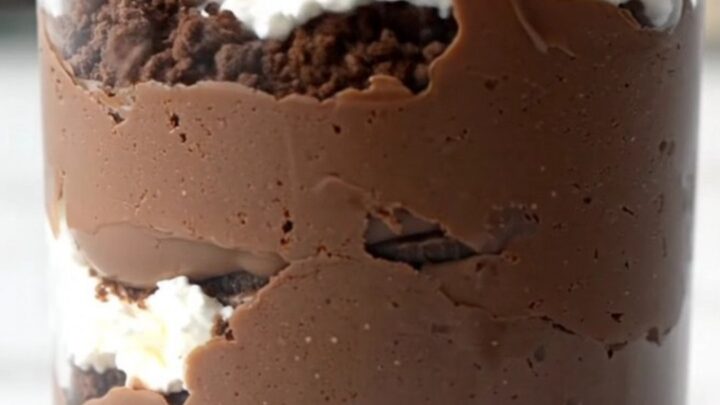 A close-up shot of a glass cup filled with layers of crushed Oreos, dark chocolate pudding, and glossy ganache.