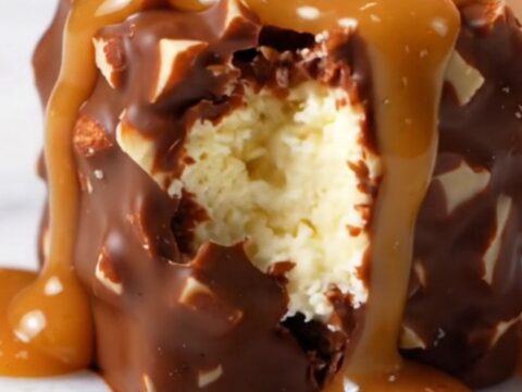 Extreme close-up of a frozen cheesecake bite on a stick with a snappy, glossy dark chocolate shell and almond pieces.