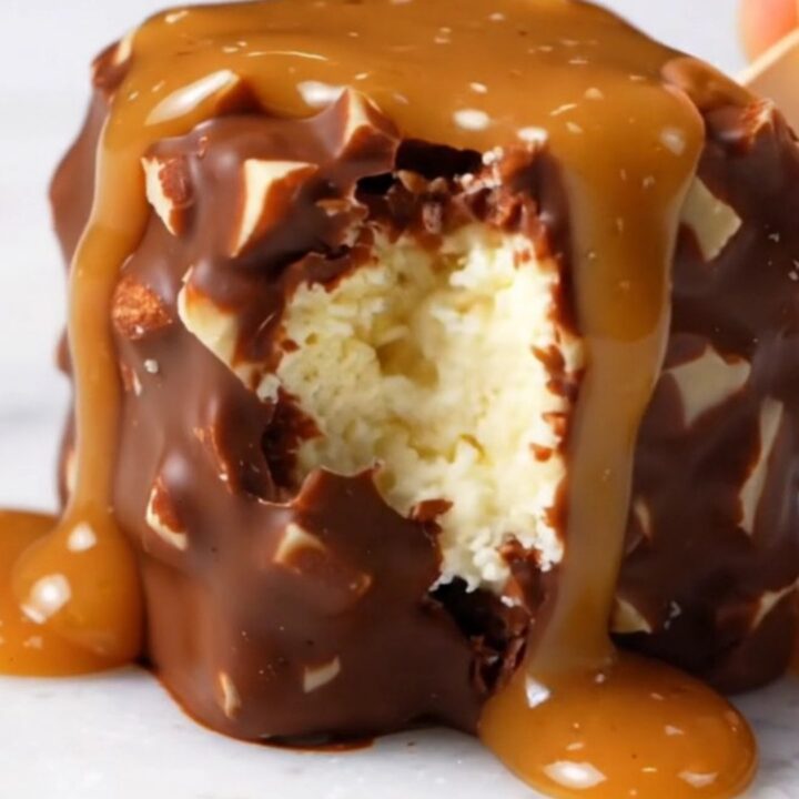 Extreme close-up of a frozen cheesecake bite on a stick with a snappy, glossy dark chocolate shell and almond pieces.