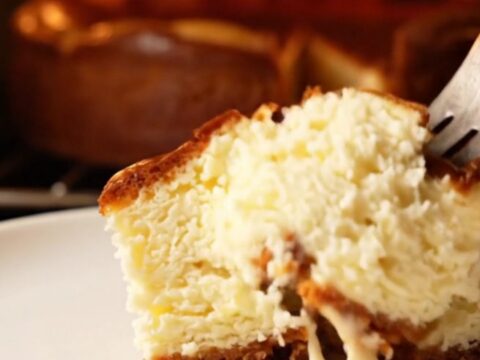 A slice of Basque cheesecake with a golden-brown charred top and a soft, creamy center on a dark plate.