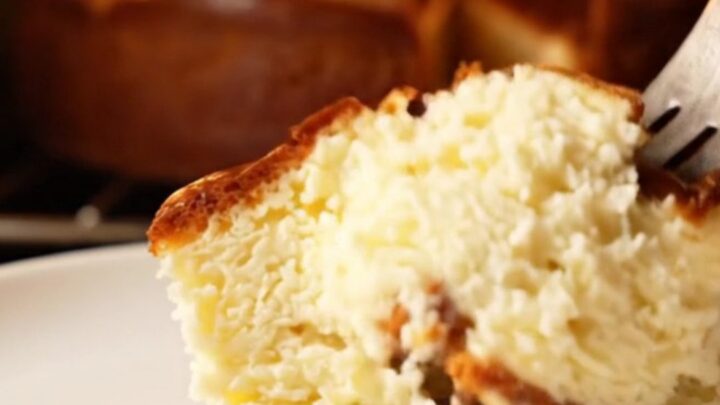 A slice of Basque cheesecake with a golden-brown charred top and a soft, creamy center on a dark plate.