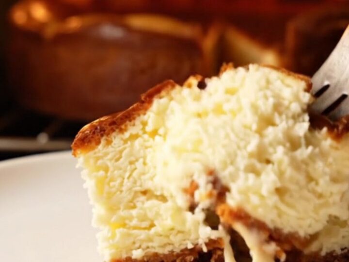 A slice of Basque cheesecake with a golden-brown charred top and a soft, creamy center on a dark plate.