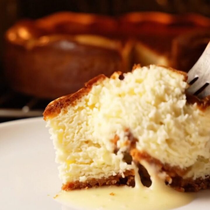 A slice of Basque cheesecake with a golden-brown charred top and a soft, creamy center on a dark plate.