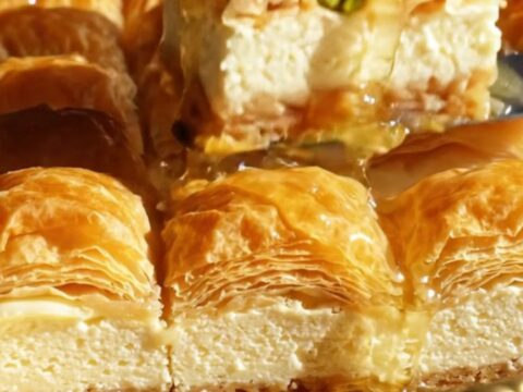 A close-up of a crispy baklava cheesecake bar showing flaky layers and a creamy center.