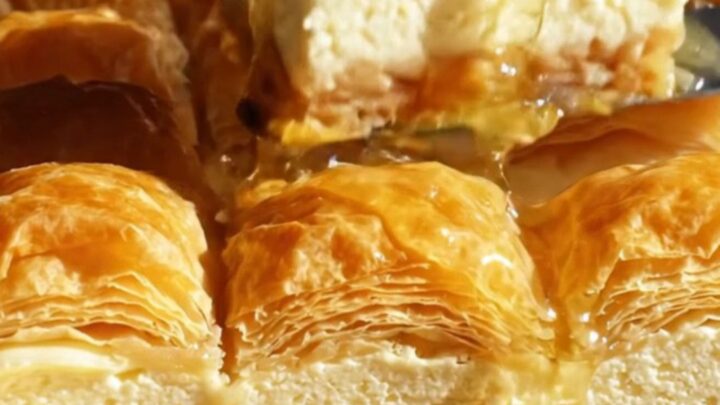 A close-up of a crispy baklava cheesecake bar showing flaky layers and a creamy center.