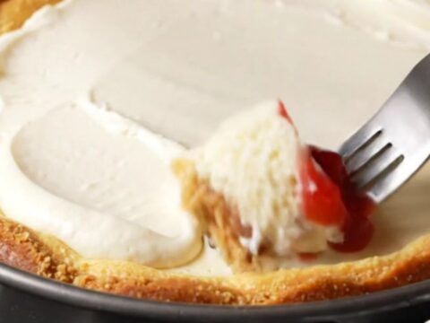 A slice of dense New York cheesecake topped with strawberry compote on a white plate.