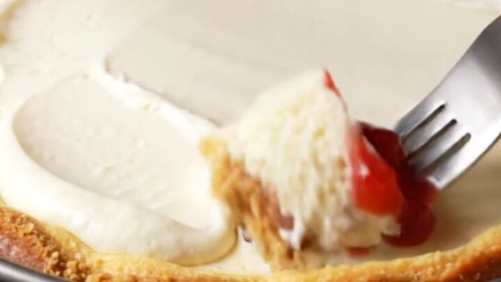 A slice of dense New York cheesecake topped with strawberry compote on a white plate.