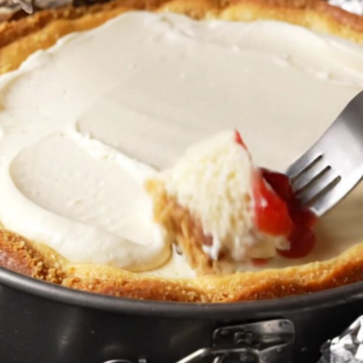 A slice of dense New York cheesecake topped with strawberry compote on a white plate.