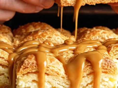 A close-up of a golden, crispy churro cheesecake square with a creamy center and a drizzle of dulce de leche.