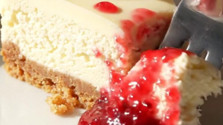A slice of white chocolate cheesecake on a marble counter with a beautiful red raspberry marble swirl.