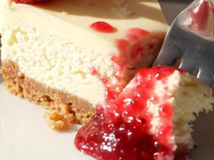 A slice of white chocolate cheesecake on a marble counter with a beautiful red raspberry marble swirl.