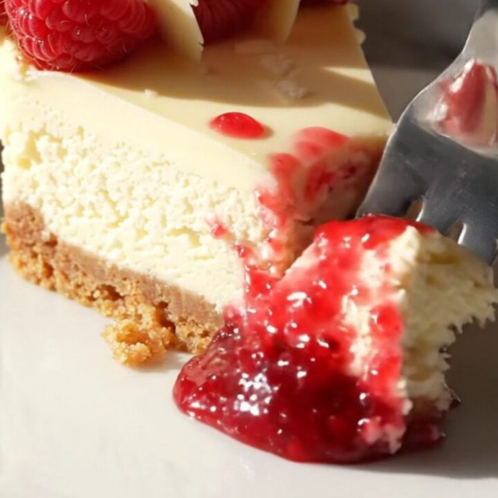 A slice of white chocolate cheesecake on a marble counter with a beautiful red raspberry marble swirl.