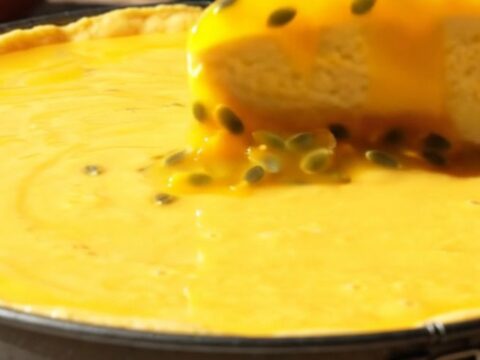 A vibrant mango cheesecake with a glossy passionfruit glaze and crunchy coconut crust on a sunlit veranda.
