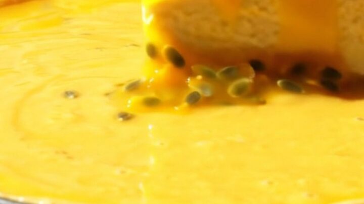 A vibrant mango cheesecake with a glossy passionfruit glaze and crunchy coconut crust on a sunlit veranda.