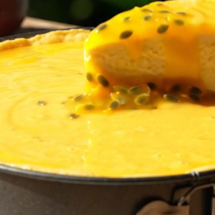 A vibrant mango cheesecake with a glossy passionfruit glaze and crunchy coconut crust on a sunlit veranda.