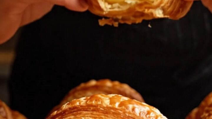A golden, flaky butter croissant sliced in half, revealing an intricate and airy honeycomb interior structure.