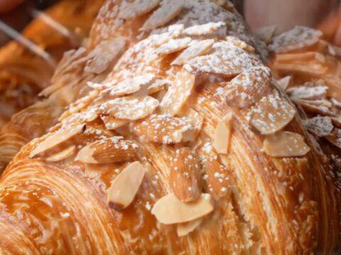 A close-up shot of a twice-baked almond croissant with a golden, toasted almond crust dusted with powdered sugar.