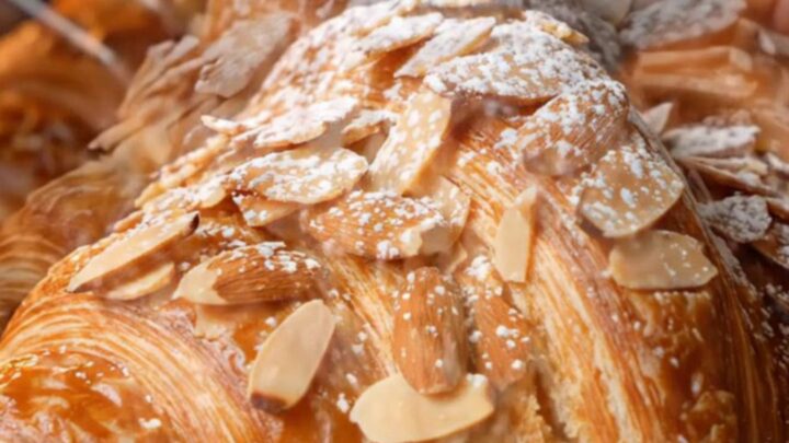 A close-up shot of a twice-baked almond croissant with a golden, toasted almond crust dusted with powdered sugar.