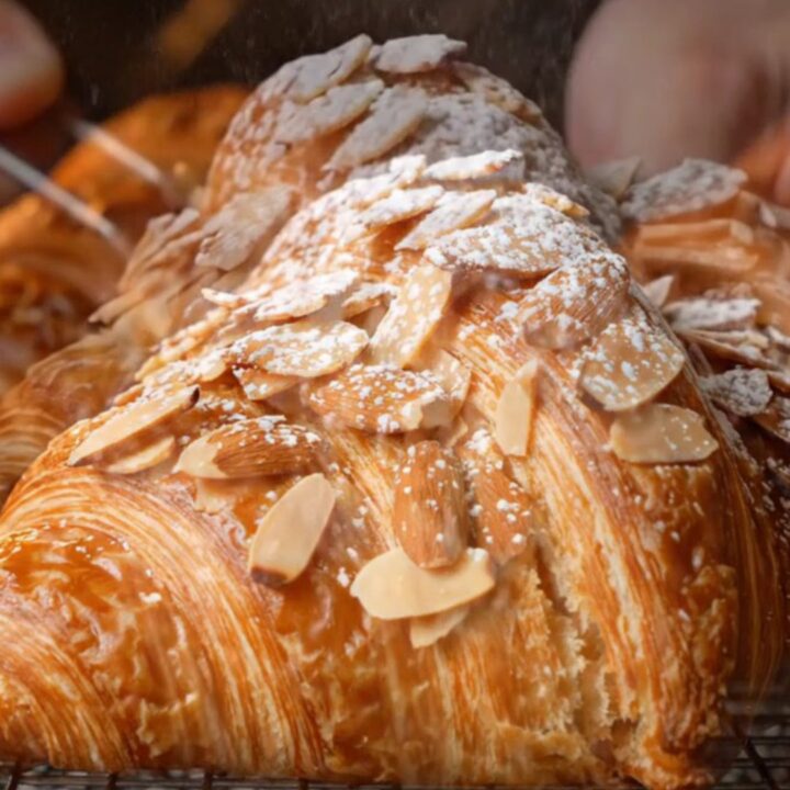 A close-up shot of a twice-baked almond croissant with a golden, toasted almond crust dusted with powdered sugar.