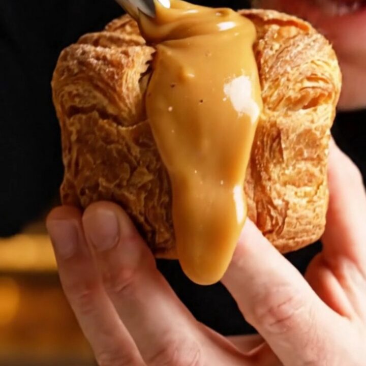 A close-up of a golden brown, flaky cinnamon sugar cruffin with a thick