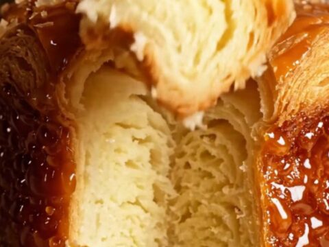 A close-up of a freshly baked Kouign-Amann showing a dark, mirror-glossy caramelized crust and flaky butter layers.