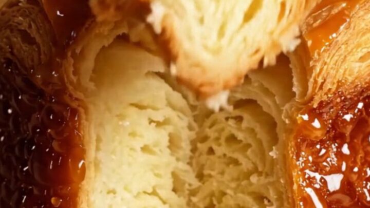 A close-up of a freshly baked Kouign-Amann showing a dark, mirror-glossy caramelized crust and flaky butter layers.
