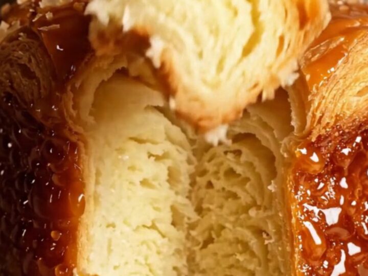A close-up of a freshly baked Kouign-Amann showing a dark, mirror-glossy caramelized crust and flaky butter layers.