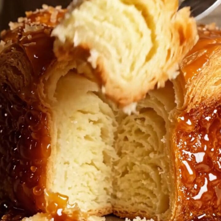 A close-up of a freshly baked Kouign-Amann showing a dark, mirror-glossy caramelized crust and flaky butter layers.
