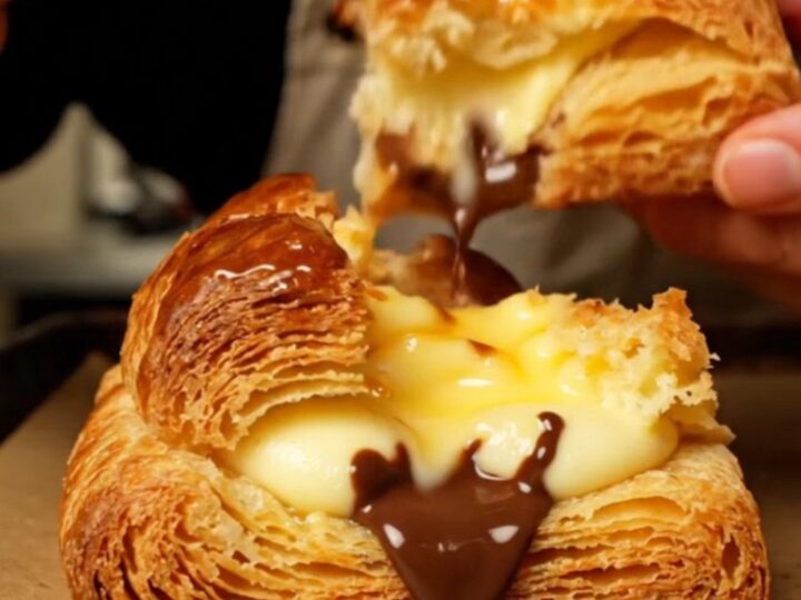 A close-up of a golden, crispy Pain Suisse showing layers of pastry, vanilla cream, and dark chocolate.