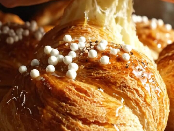 A close-up shot of a golden-brown Swedish cardamom bun with pearl sugar on a wooden table.