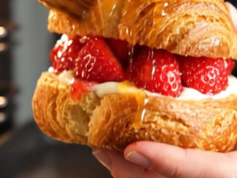 A close-up of a diamond-shaped strawberry danish with visible ruby-red laminated layers and glistening fruit.