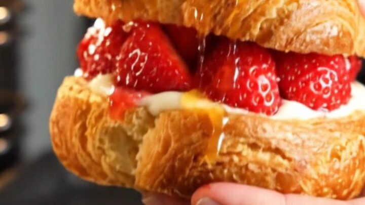 A close-up of a diamond-shaped strawberry danish with visible ruby-red laminated layers and glistening fruit.