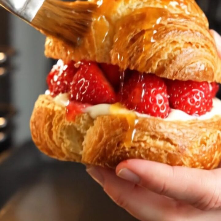 A close-up of a diamond-shaped strawberry danish with visible ruby-red laminated layers and glistening fruit.