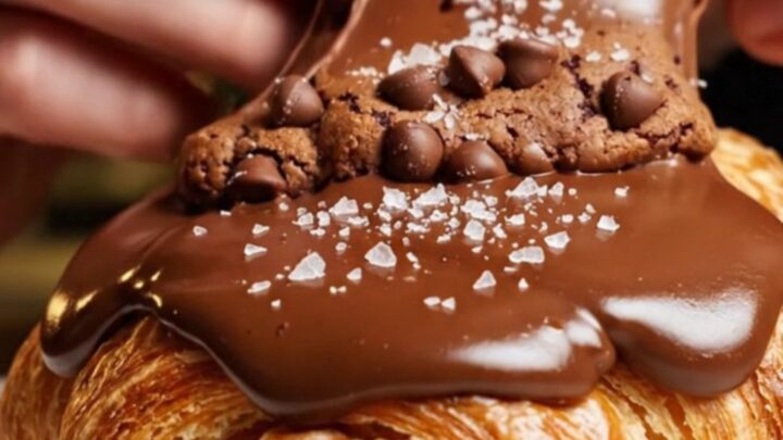 A golden-brown croissant split in half, revealing a gooey, molten chocolate chip cookie dough center.