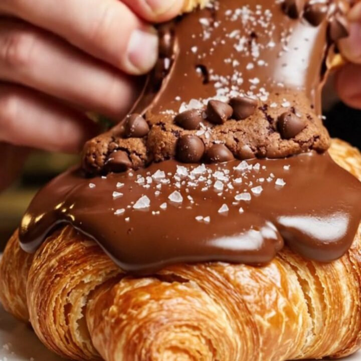 A golden-brown croissant split in half, revealing a gooey, molten chocolate chip cookie dough center.
