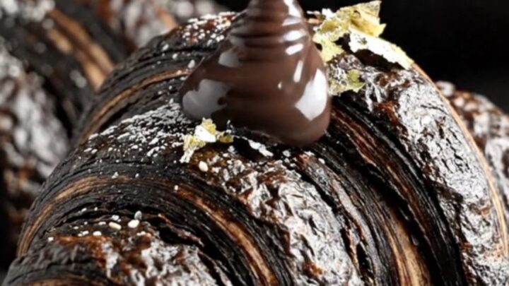 A dramatic jet-black charcoal croissant torn open to reveal a flowing black sesame lava center.