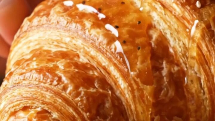 A golden, flaky everything bagel croissant drizzled with hot honey, showing a glimpse of the creamy filling inside.