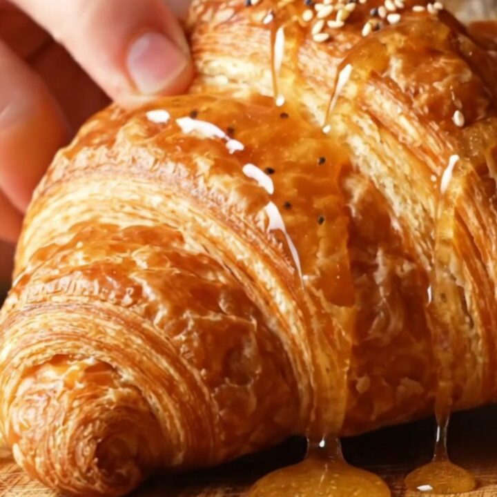 A golden, flaky everything bagel croissant drizzled with hot honey, showing a glimpse of the creamy filling inside.